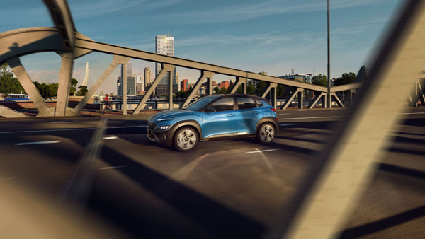 Boční pohled na nový Hyundai Kona v barvě Surfy Blue, přejíždějící most.